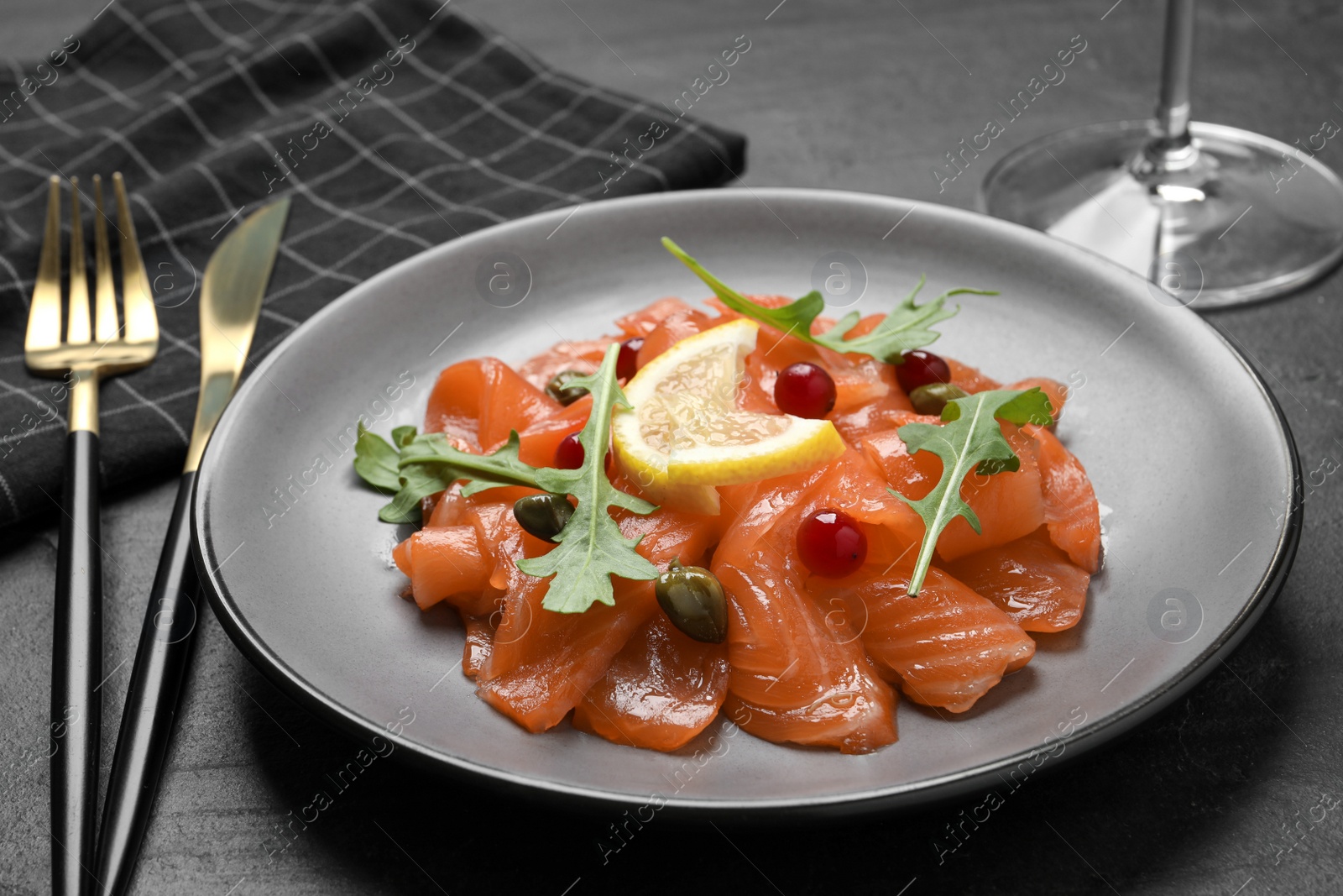 Photo of Salmon carpaccio with capers, cranberries, arugula and lemon served on black table