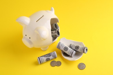 Financial savings. Broken piggy bank, dollar banknotes and coins on yellow background