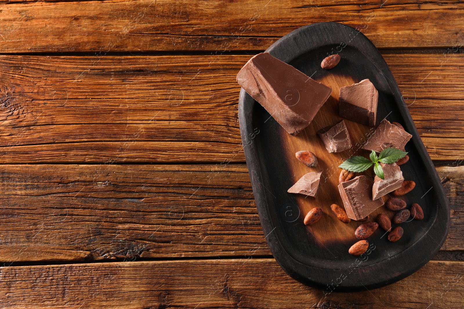 Photo of Pieces of tasty milk chocolate, mint and cocoa beans on wooden table, top view. Space for text