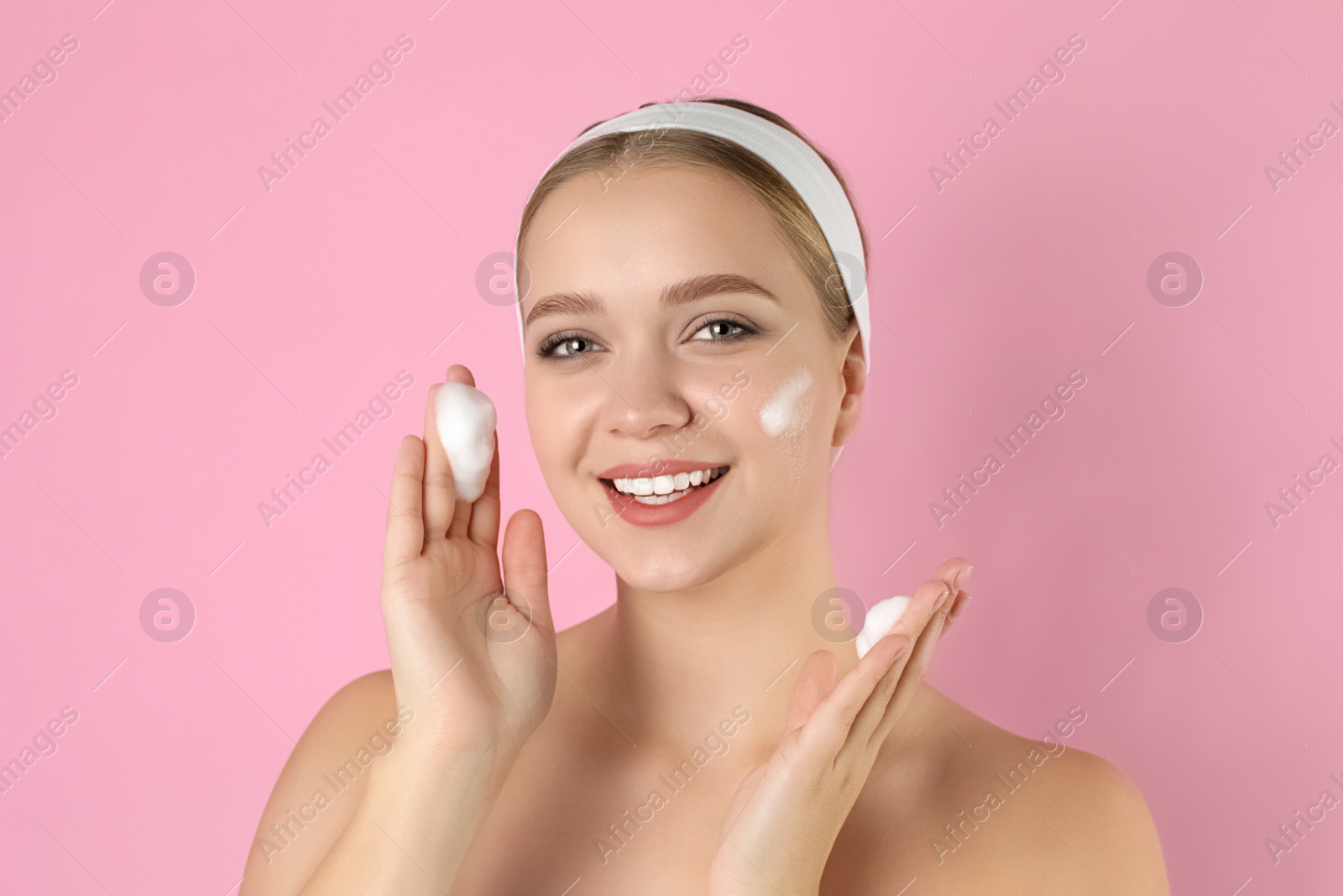 Photo of Young woman washing face with cleansing foam on pink background. Cosmetic product