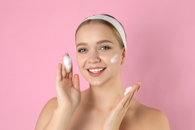 Young woman washing face with cleansing foam on pink background. Cosmetic product