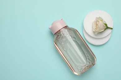 Photo of Bottlemicellar cleansing water, cotton pads and flower on turquoise background, flat lay. Space for text
