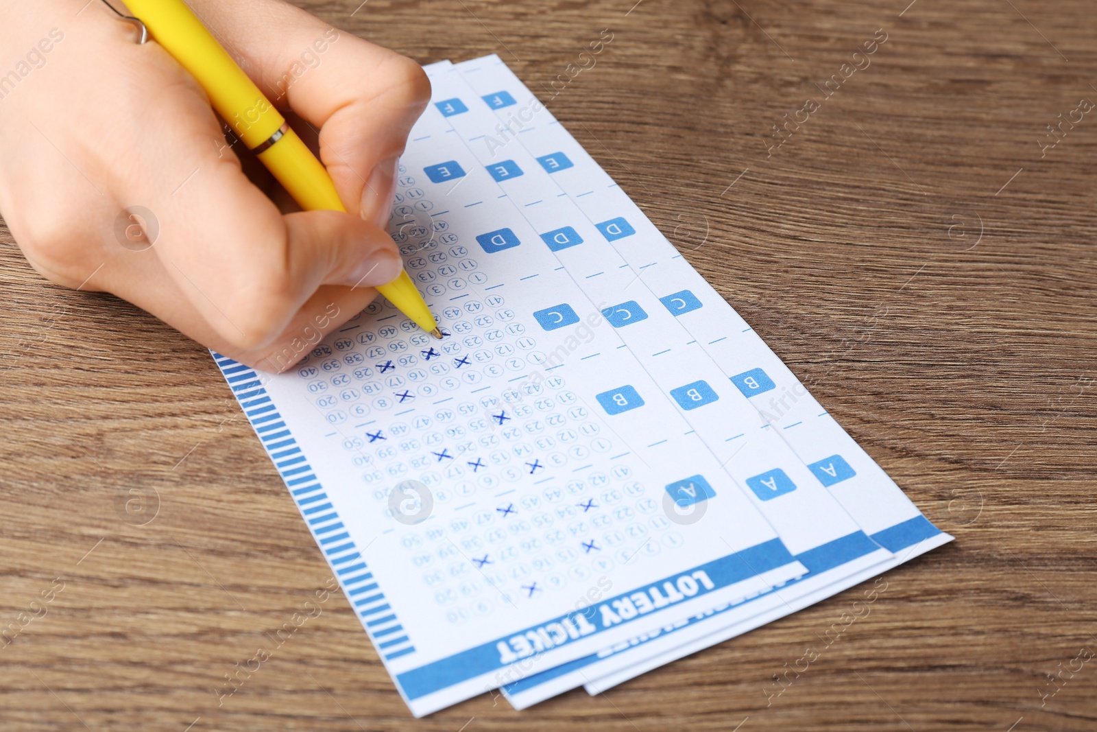 Photo of Woman filling out lottery tickets with pen on wooden table, closeup