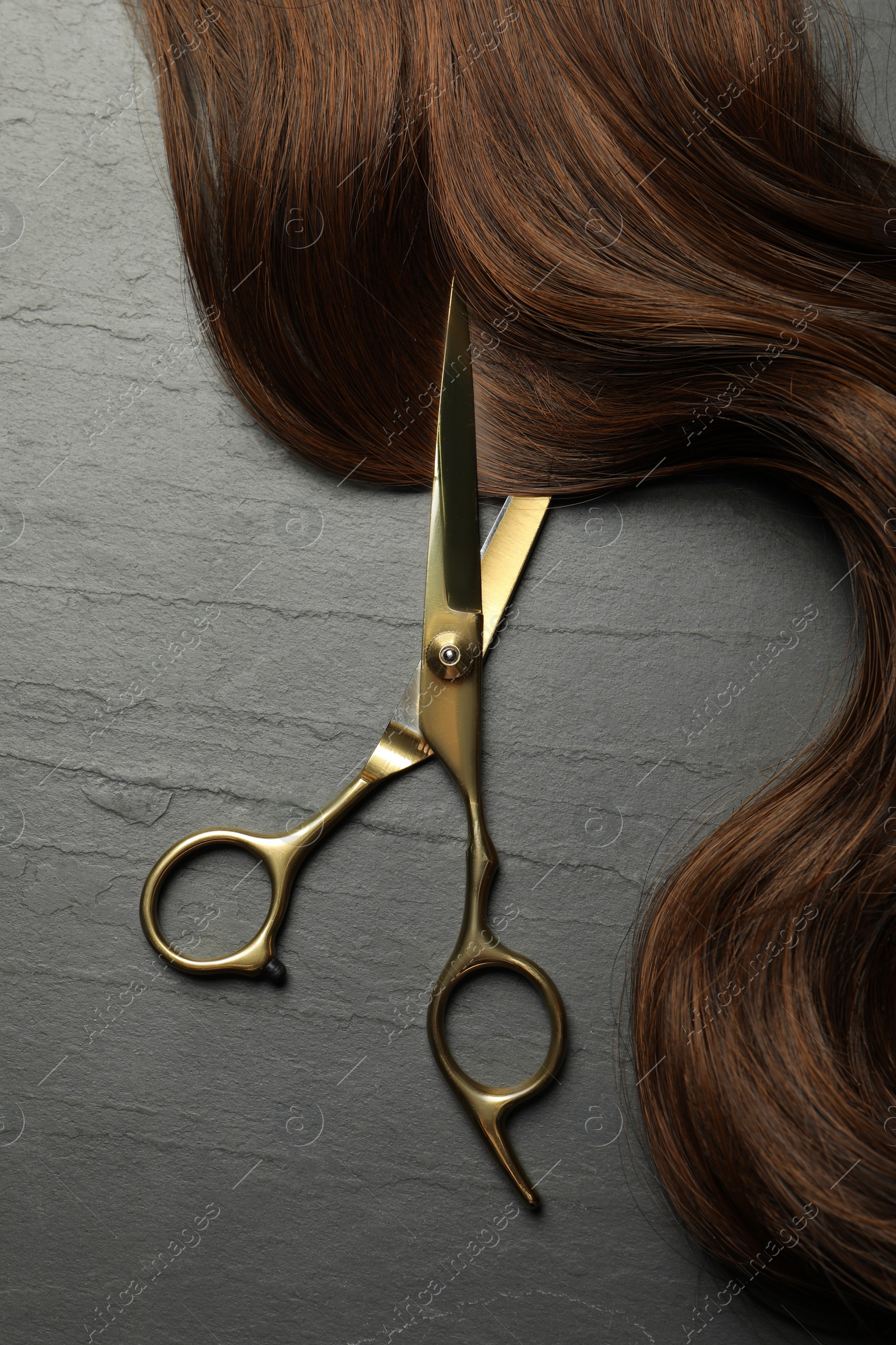 Photo of Professional hairdresser scissors with brown hair strand on dark grey table, top view
