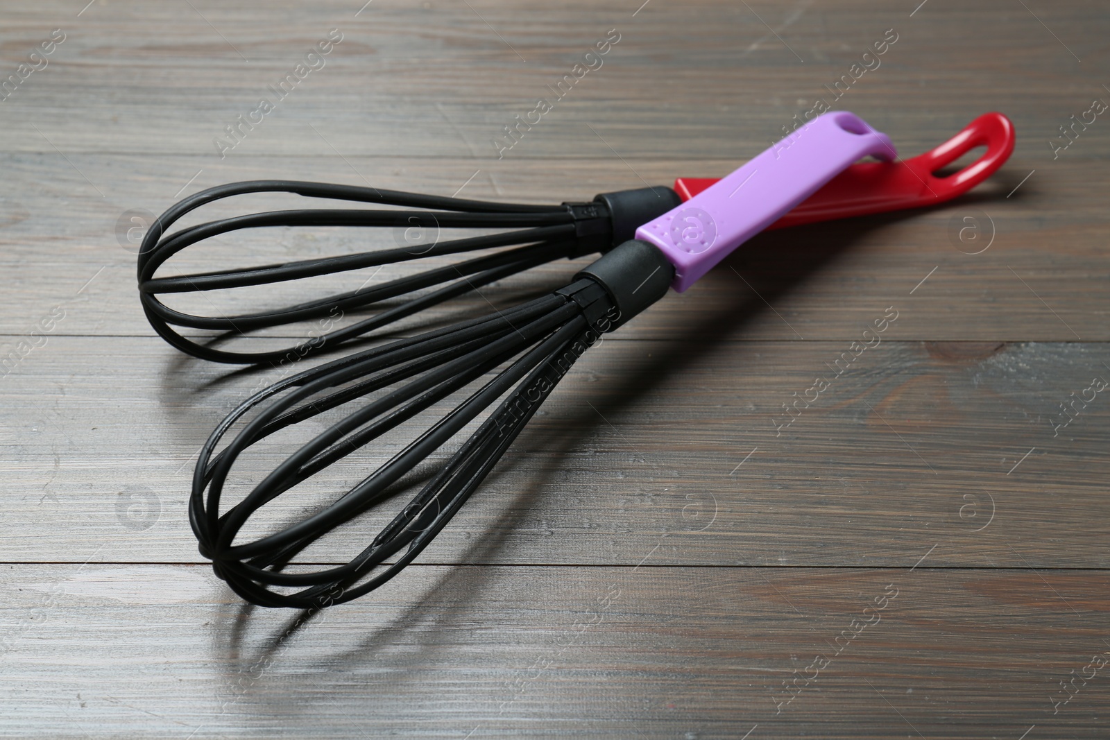 Photo of Two whisks on wooden table, closeup. Kitchen tool