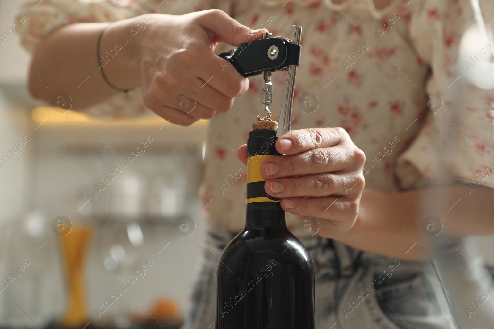 Photo of Woman opening wine bottle with corkscrew on blurred background, closeup