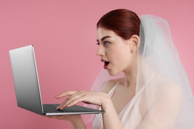 Photo of Surprised bride using laptop on pink background