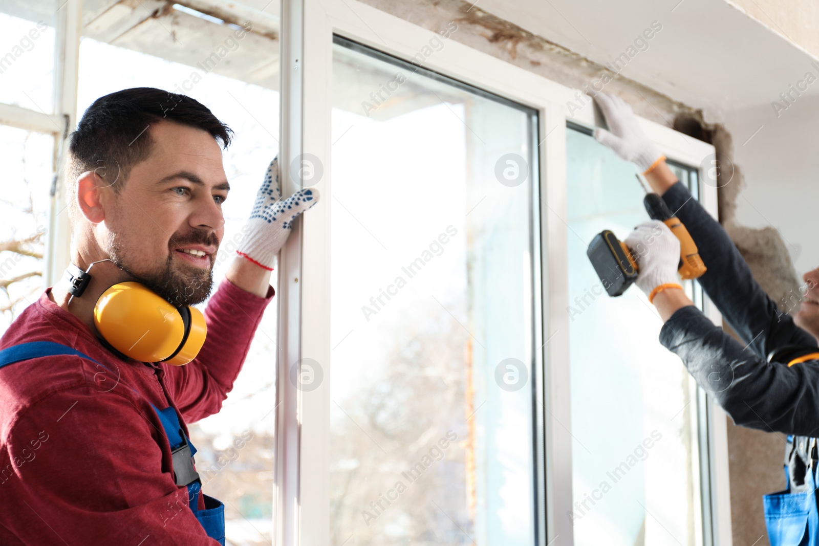 Photo of Workers in uniform installing plastic window indoors