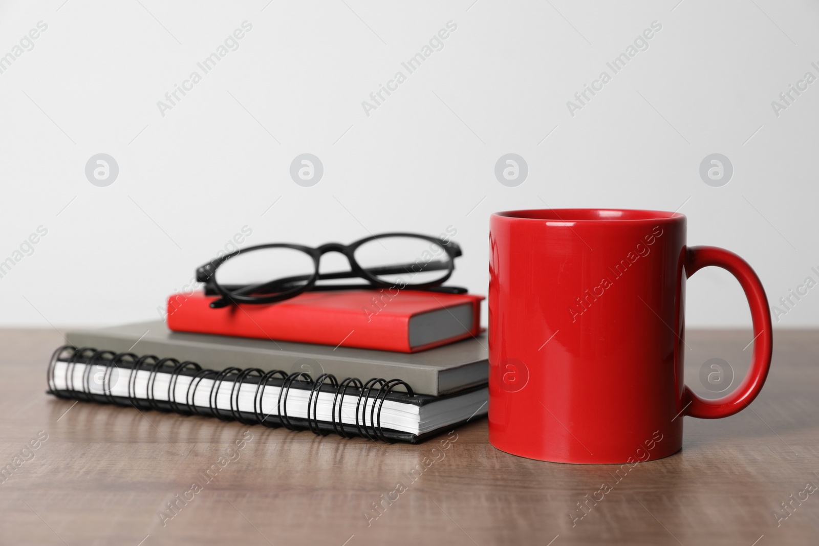 Red ceramic mug, stationery and glasses on wooden table Photo of Red ceramic mug, stationery and glasses on wooden table