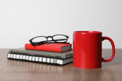 Photo of Red ceramic mug, stationery and glasses on wooden table