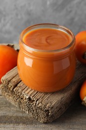 Photo of Delicious persimmon jam and fresh fruits on wooden table, closeup