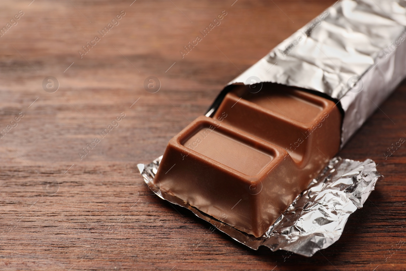 Photo of Tasty chocolate bar on wooden table, closeup. Space for text