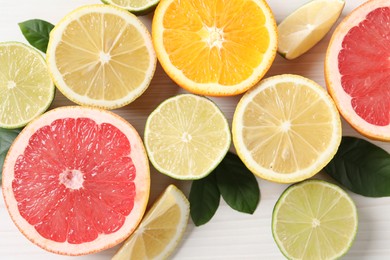 Different cut citrus fruits and leaves on white wooden table, flat lay