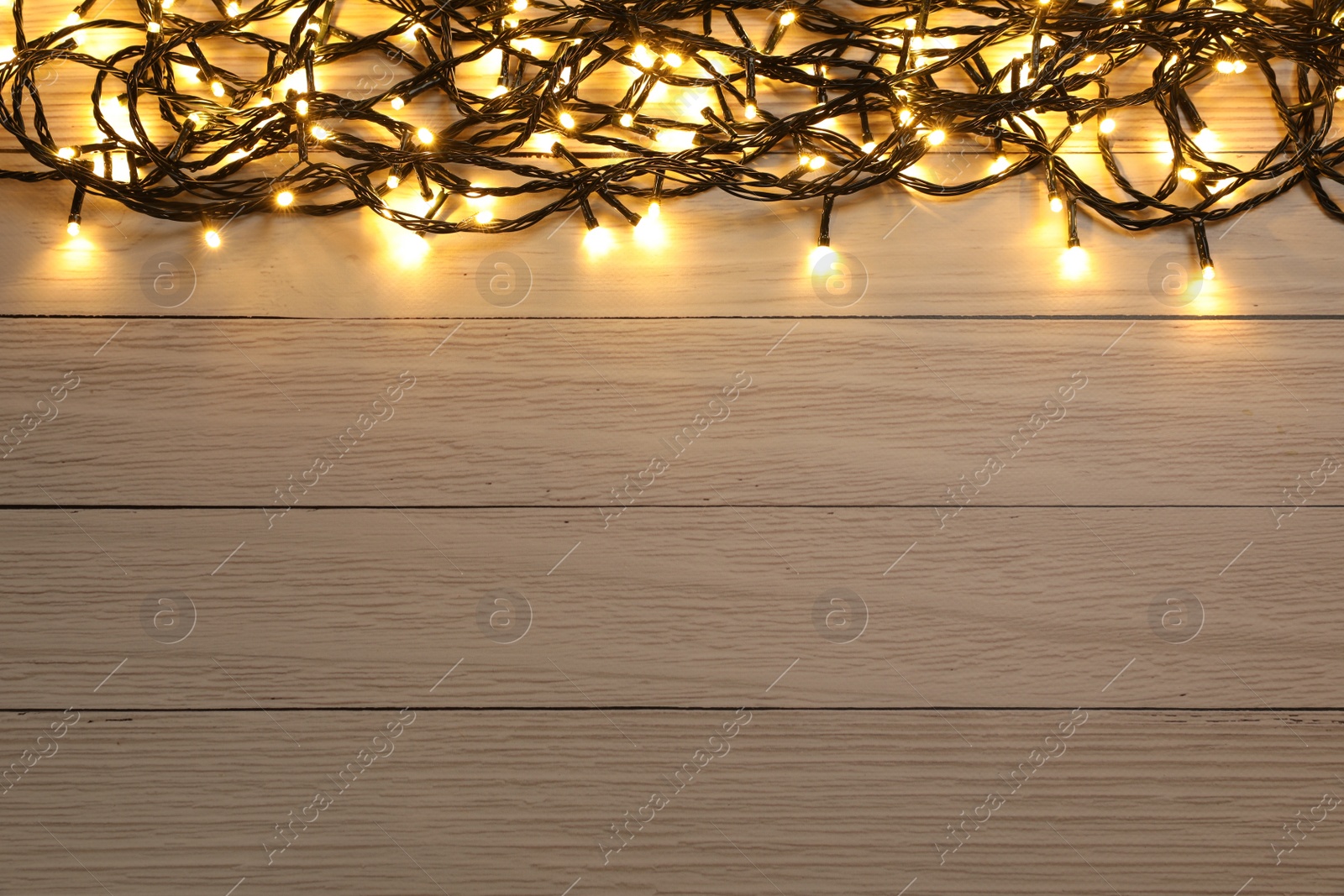 Photo of Glowing festive lights on wooden background, top view. Space for text