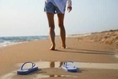 Woman left her beach slippers and walking barefoot on sandy seashore, closeup