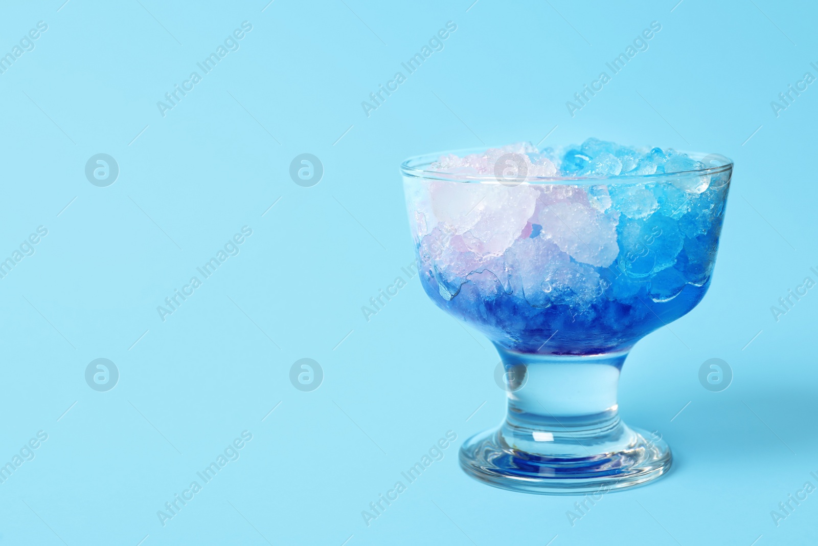 Photo of Shaving ice in glass dessert bowl on light blue background, closeup. Space for text