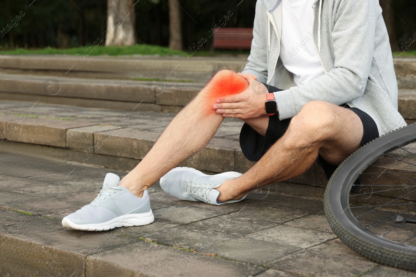 Image of Man with injured knee on steps near bicycle outdoors, closeup