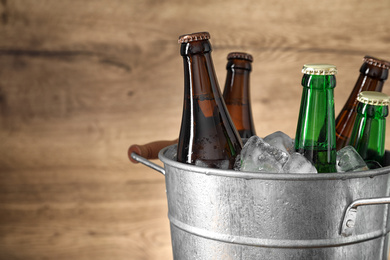 Photo of Metal bucket with beer and ice cubes on wooden background. Space for text