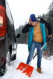 Photo of Man cleaning snow with shovel near stuck car outdoors