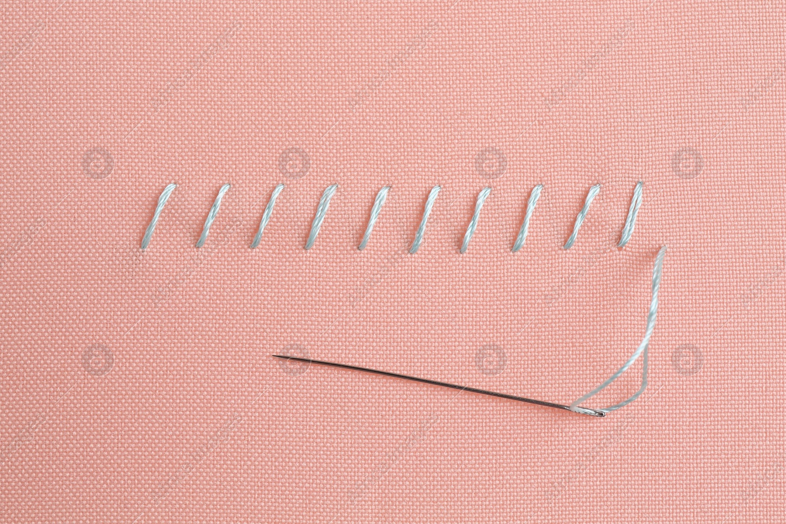 Photo of Sewing needle with thread and stitches on coral cloth, top view