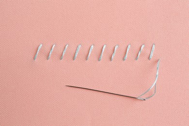 Photo of Sewing needle with thread and stitches on coral cloth, top view