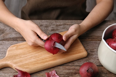 Photo of Woman peeling ripe red onion on wooden table