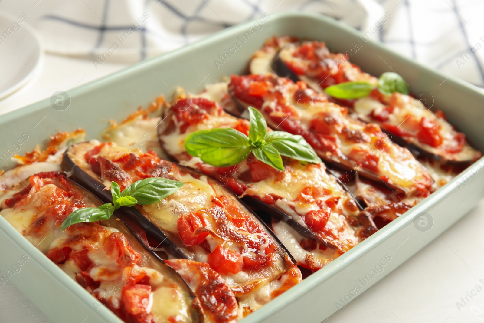 Photo of Baked eggplant with tomatoes, cheese and basil in dishware on white table, closeup