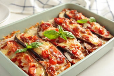 Baked eggplant with tomatoes, cheese and basil in dishware on white table, closeup