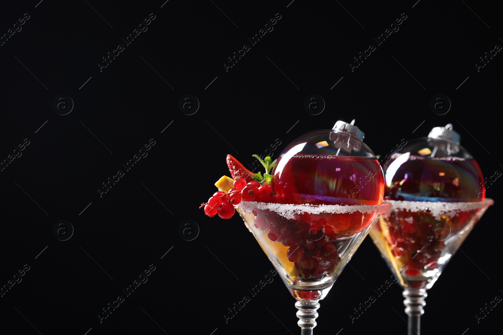 Photo of Creative presentation of Christmas Sangria cocktail in baubles and glasses on black background, closeup. Space for text