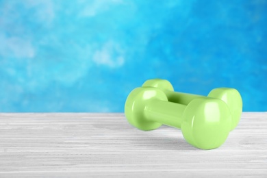 Photo of Stylish dumbbells on table against color background, space for text. Fitness equipment