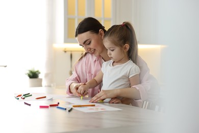 Photo of Mother and her little daughter drawing with colorful markers at table in kitchen