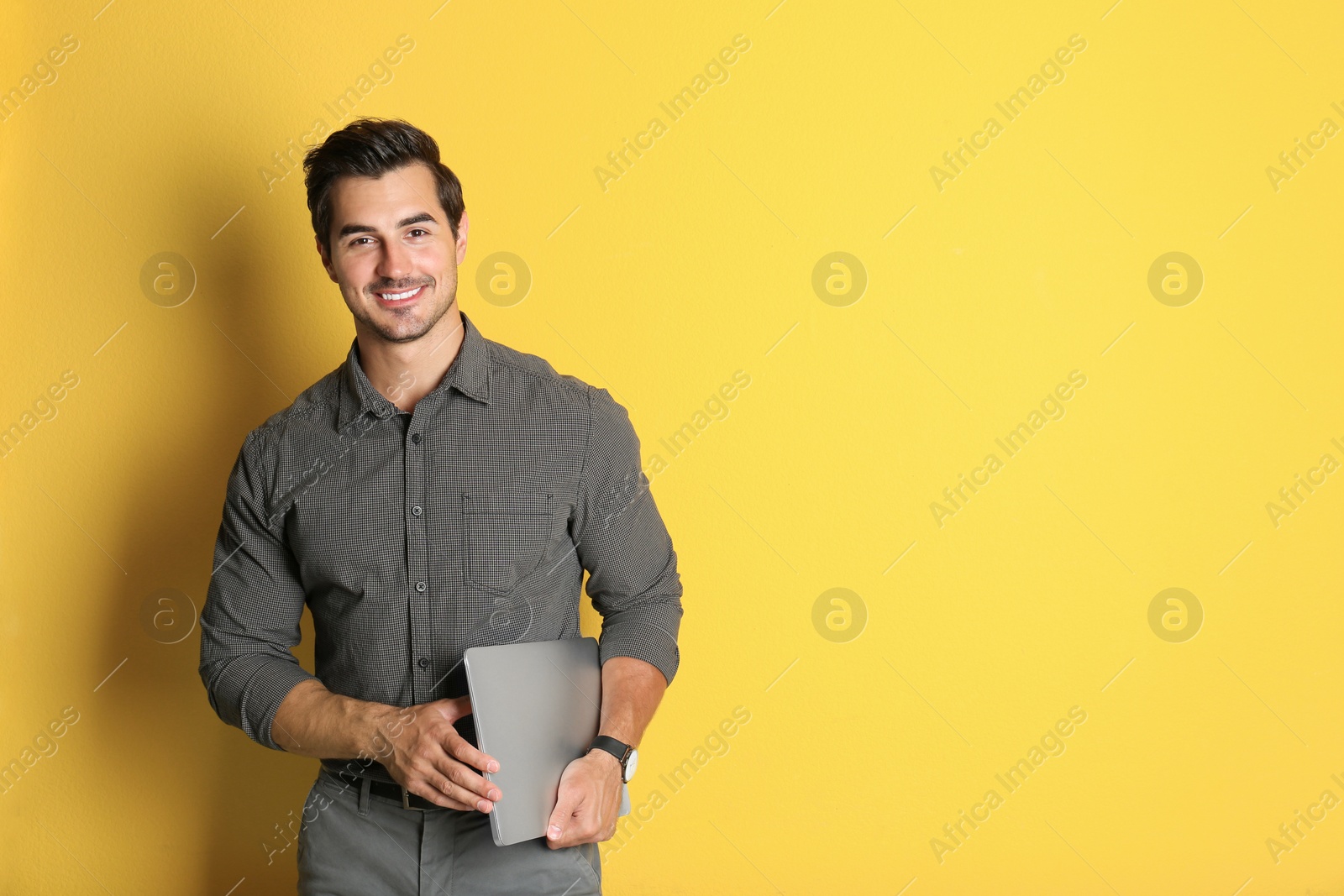 Photo of Young male teacher with laptop on yellow background. Space for text