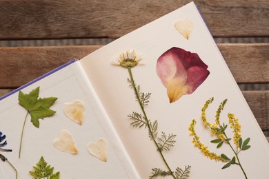 Photo of Book with dried flowers and leaves on wooden table, top view