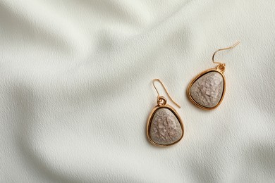 Photo of Elegant earrings on white fabric, flat lay with space for text. Stylish bijouterie