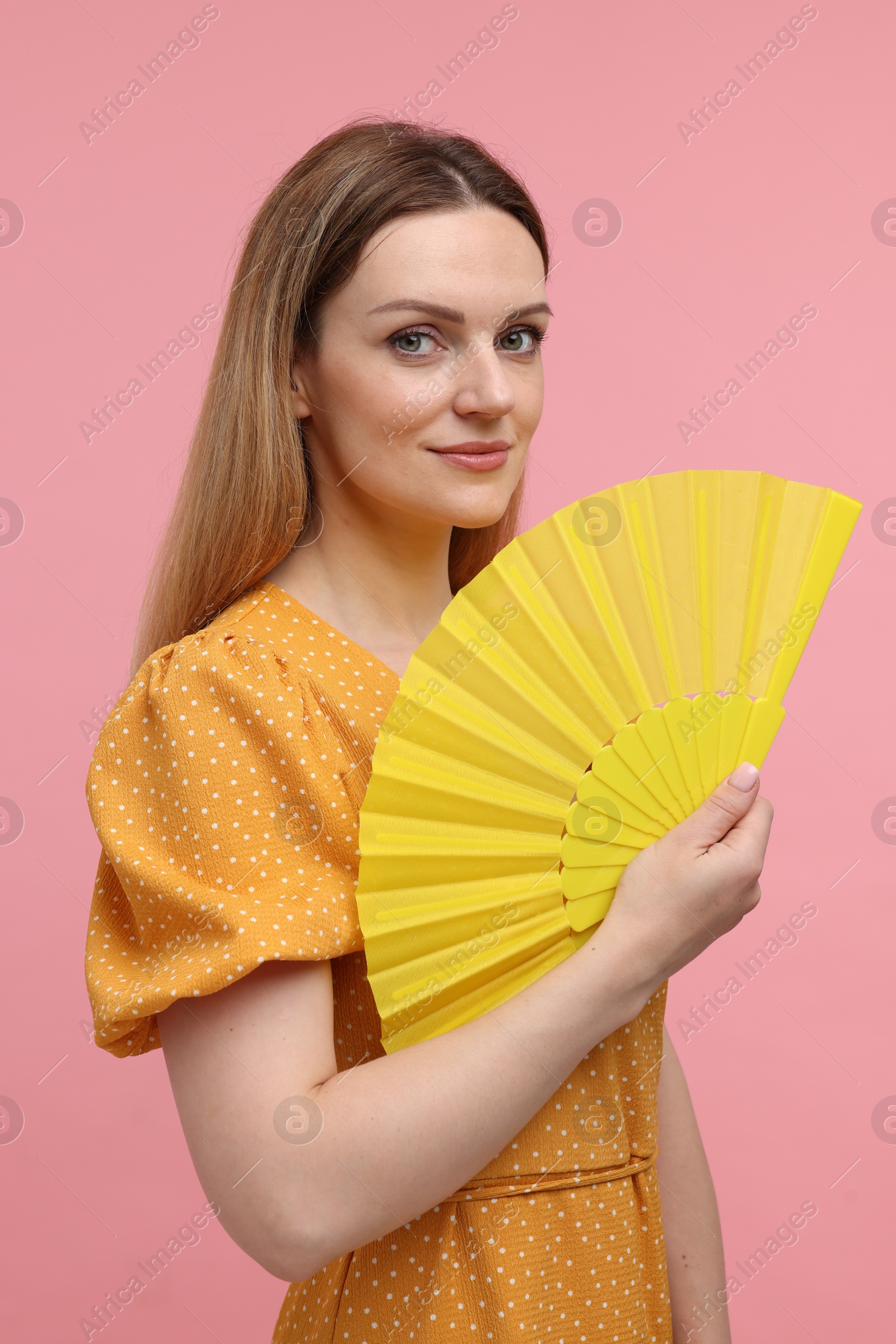 Photo of Beautiful woman with yellow hand fan on pink background