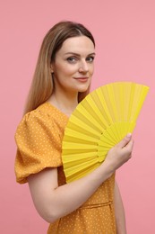 Photo of Beautiful woman with yellow hand fan on pink background
