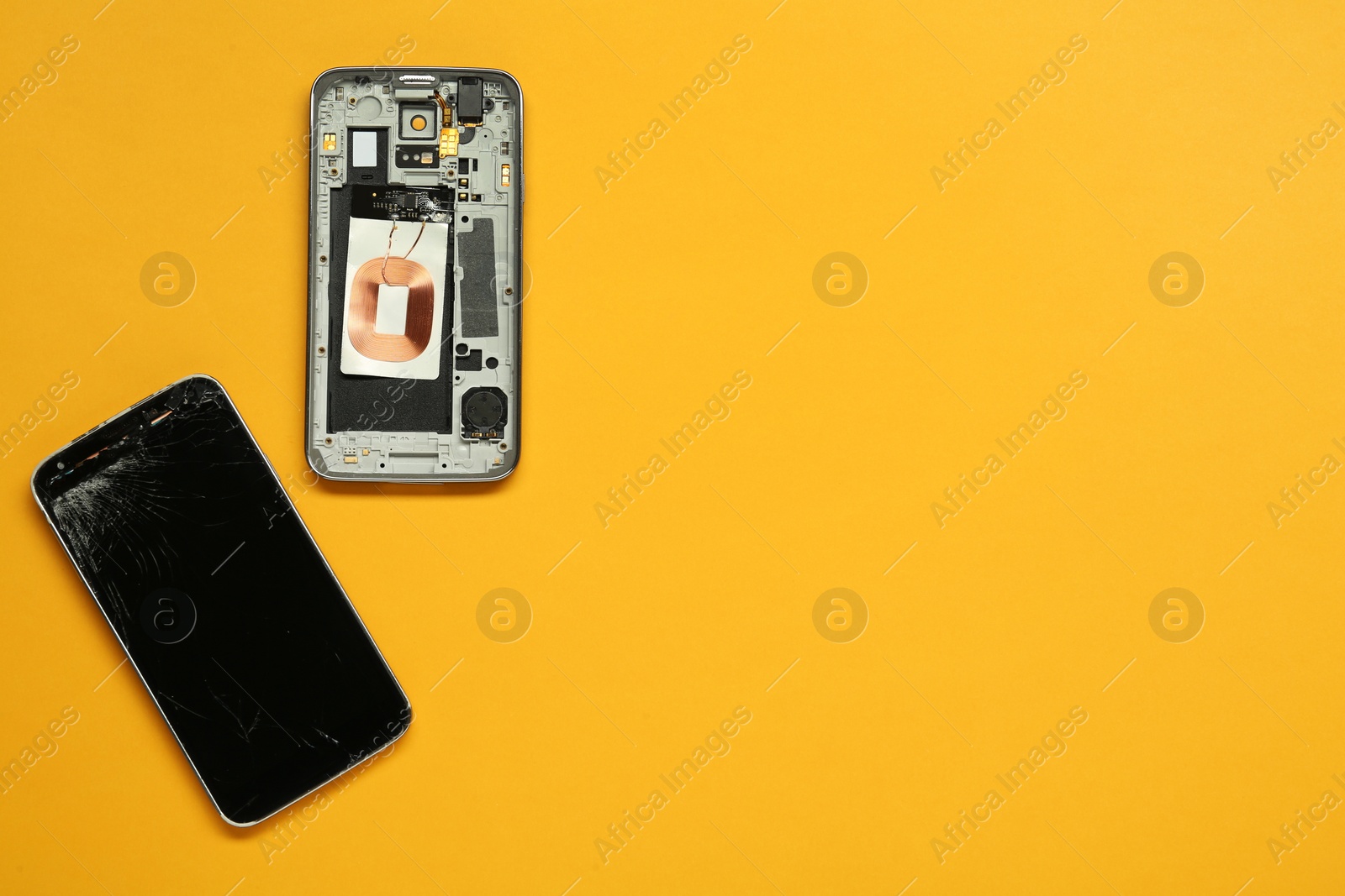 Photo of Damaged smartphone on orange background, flat lay with space for text. Device repairing