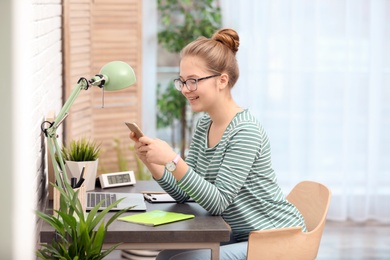 Photo of Pretty teenage girl using mobile phone at table in room