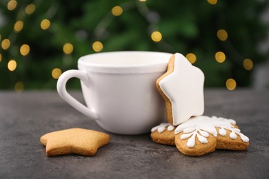 Decorated cookies and hot drink on grey table against blurred Christmas lights