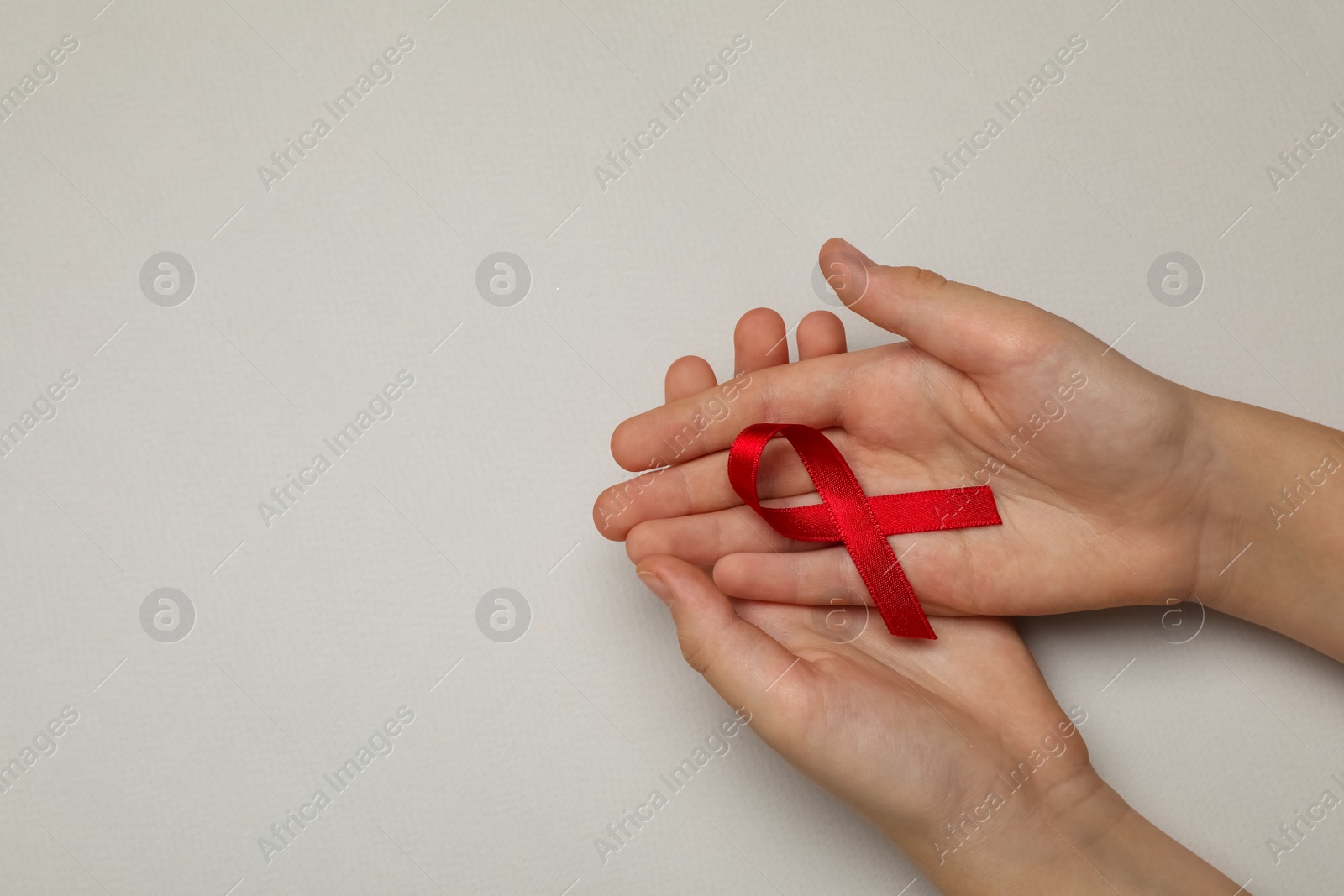 Photo of Little girl holding red ribbon on beige background, top view with space for text. AIDS disease awareness