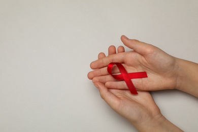 Photo of Little girl holding red ribbon on beige background, top view with space for text. AIDS disease awareness