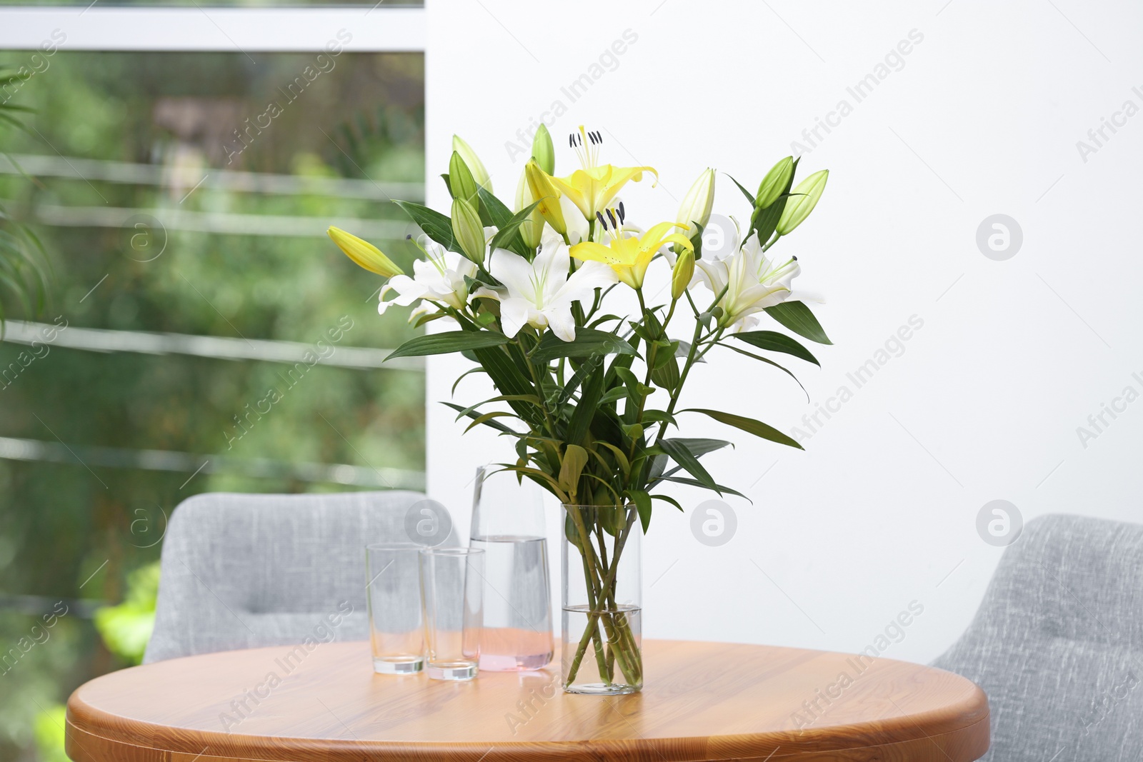 Photo of Vase with bouquet of beautiful lilies on wooden table indoors