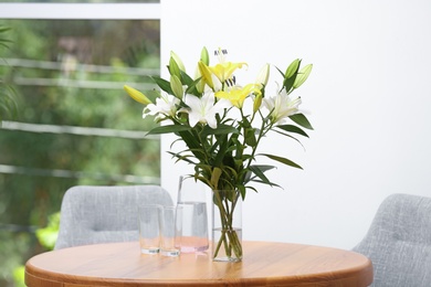 Vase with bouquet of beautiful lilies on wooden table indoors