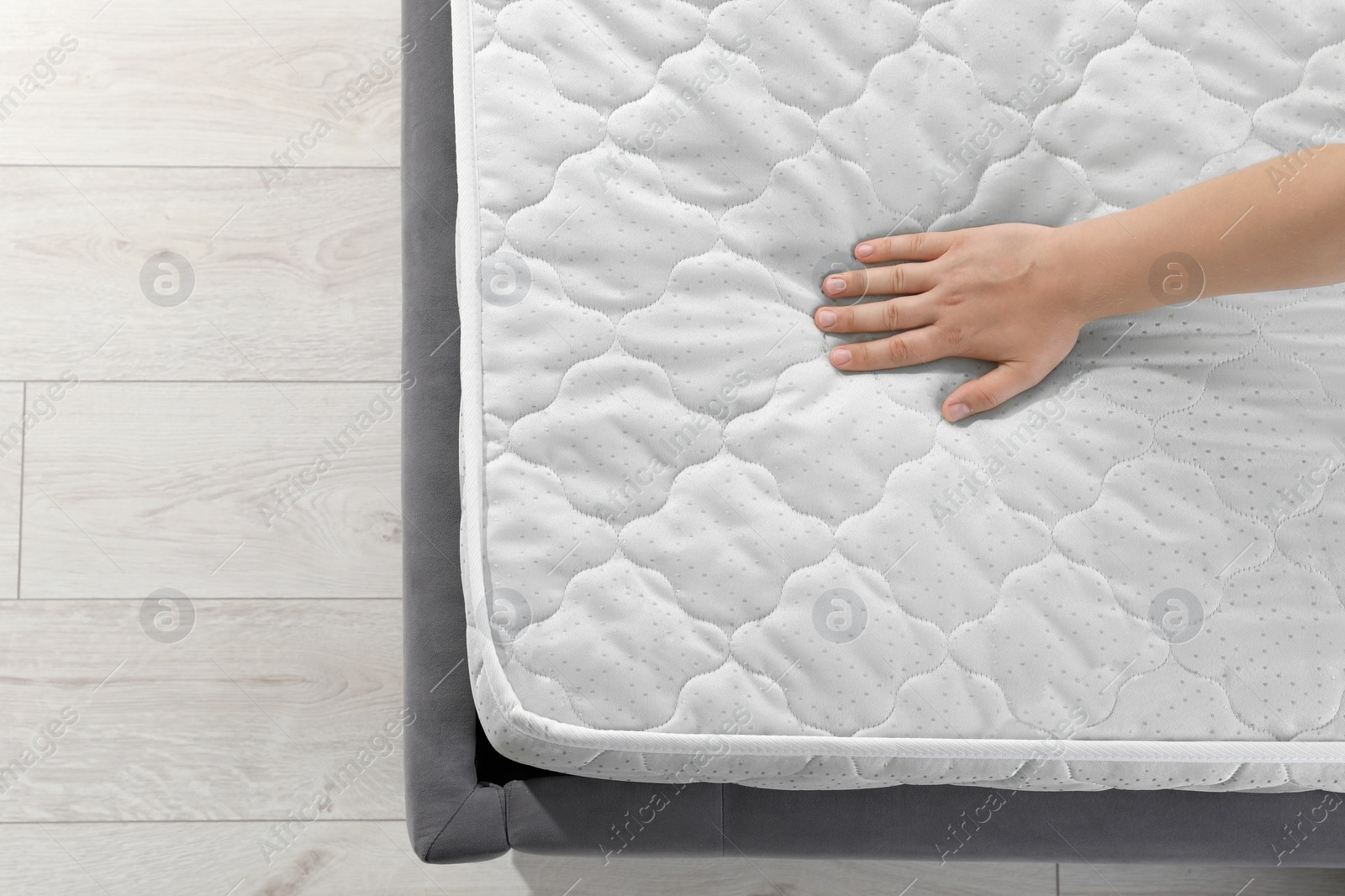 Photo of Woman touching soft light green mattress on bed, top view