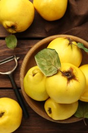 Tasty ripe quince fruits in bowl and peeler on wooden table, flat lay