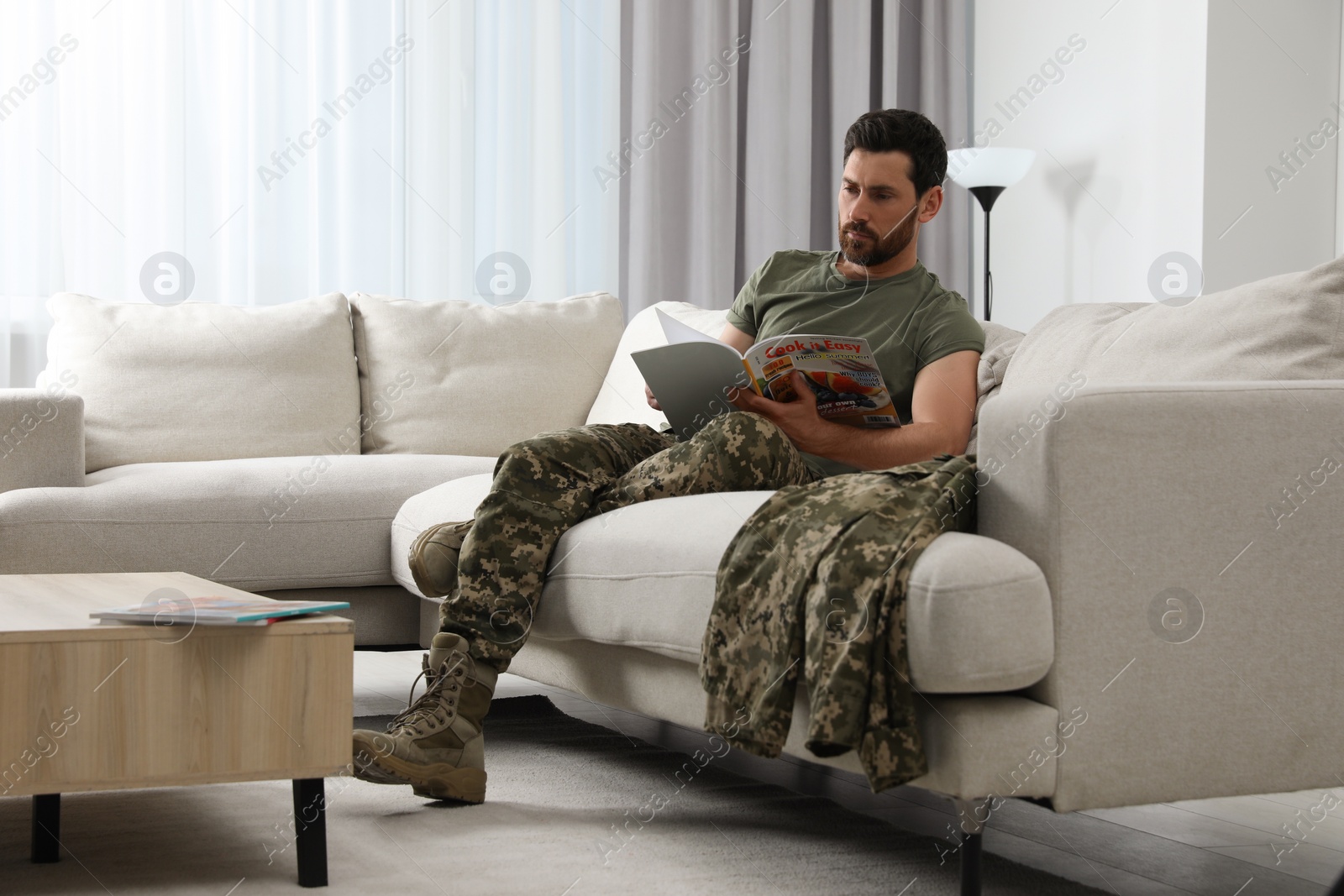 Photo of Soldier reading magazine on sofa in living room. Military service