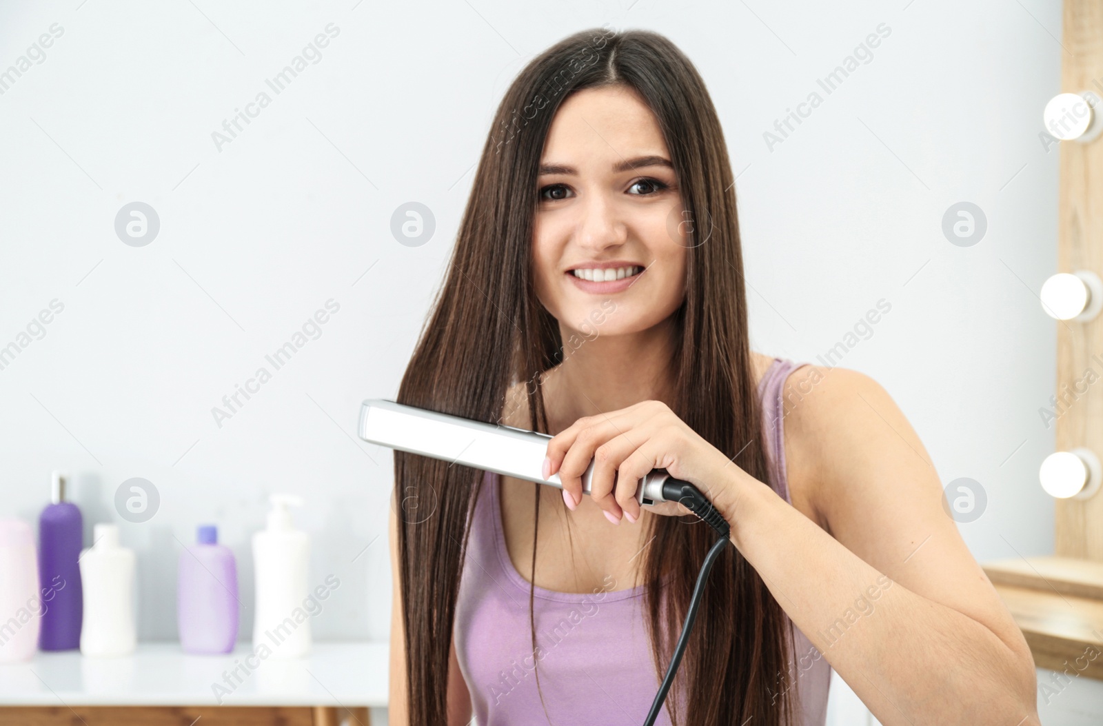 Photo of Young woman using hair iron indoors, space for text