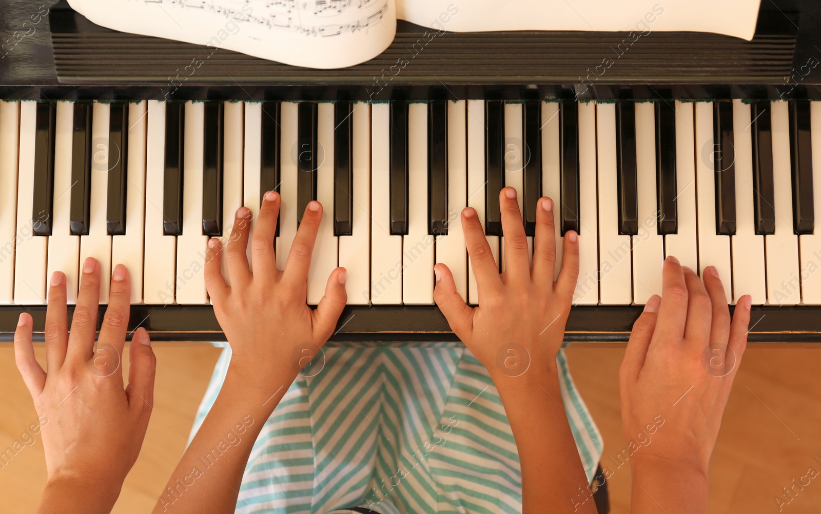 Photo of Young woman teaching little girl to play piano indoors, top view