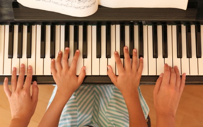 Young woman teaching little girl to play piano indoors, top view