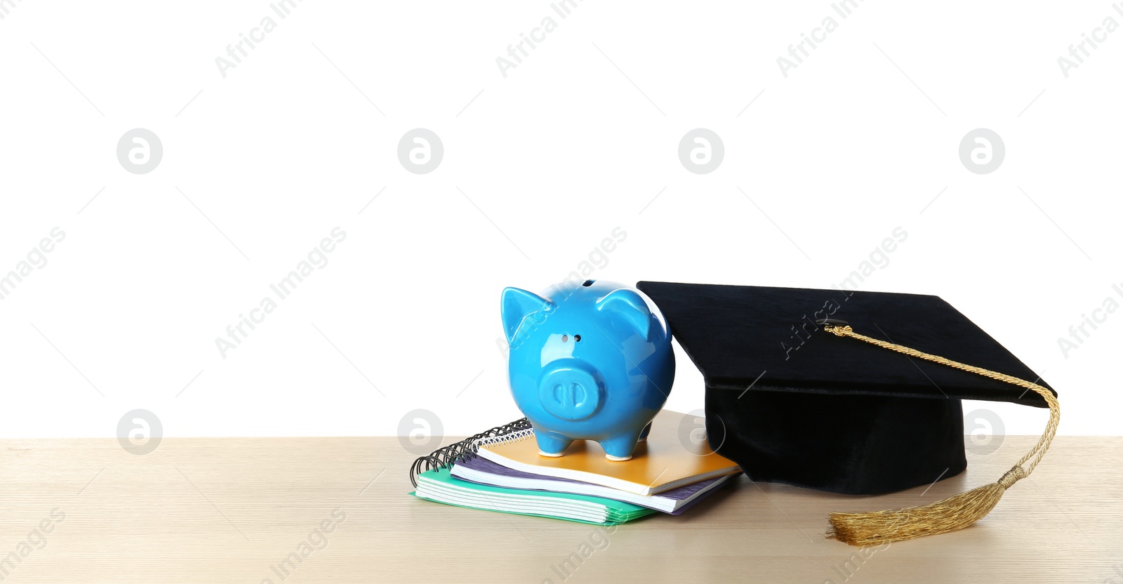 Photo of Graduation hat with piggy bank and notebooks on table against white background